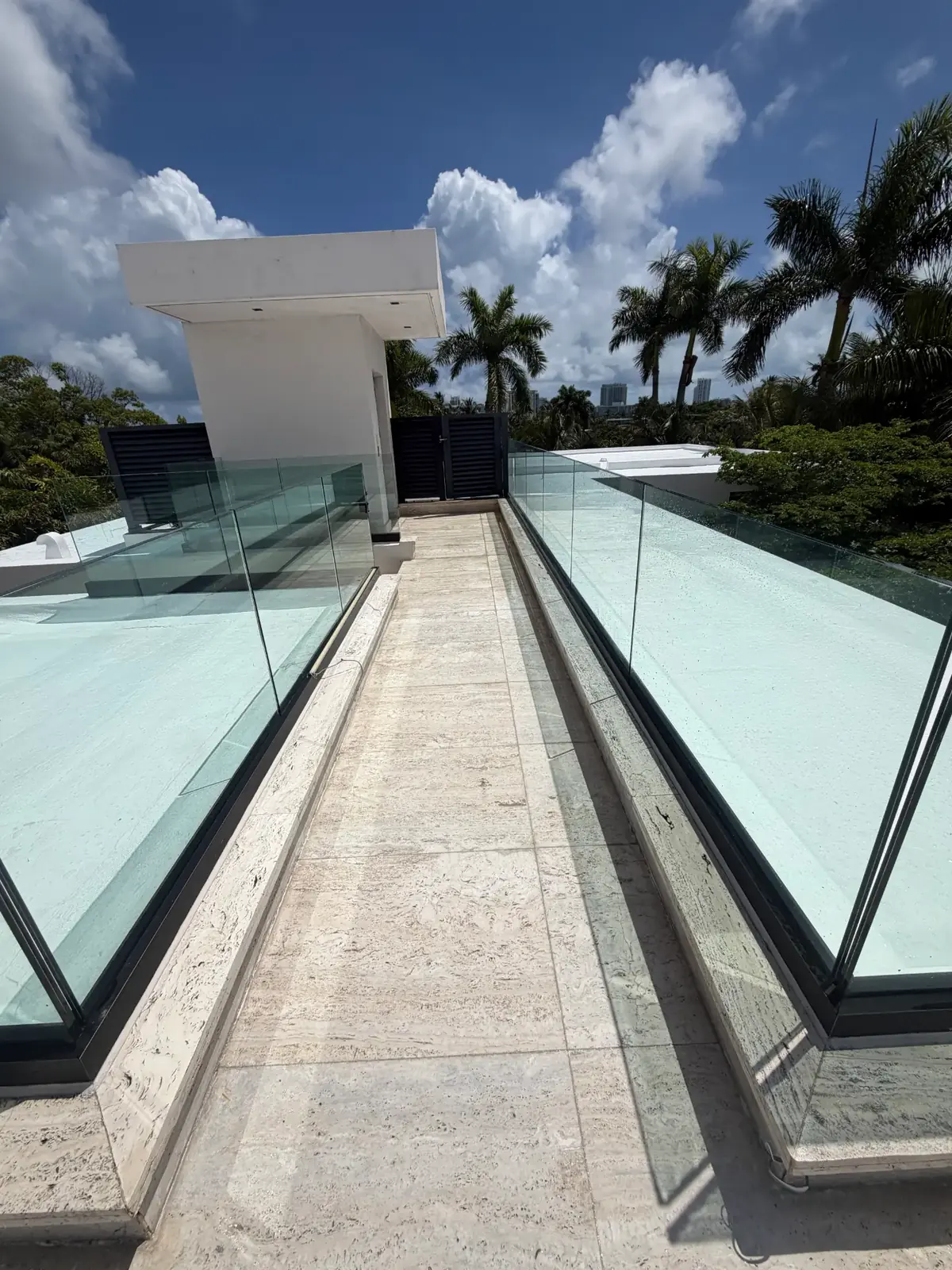 Clean travertine rooftop deck walkway between glass railings at a Miami Beach estate after stone and paver care