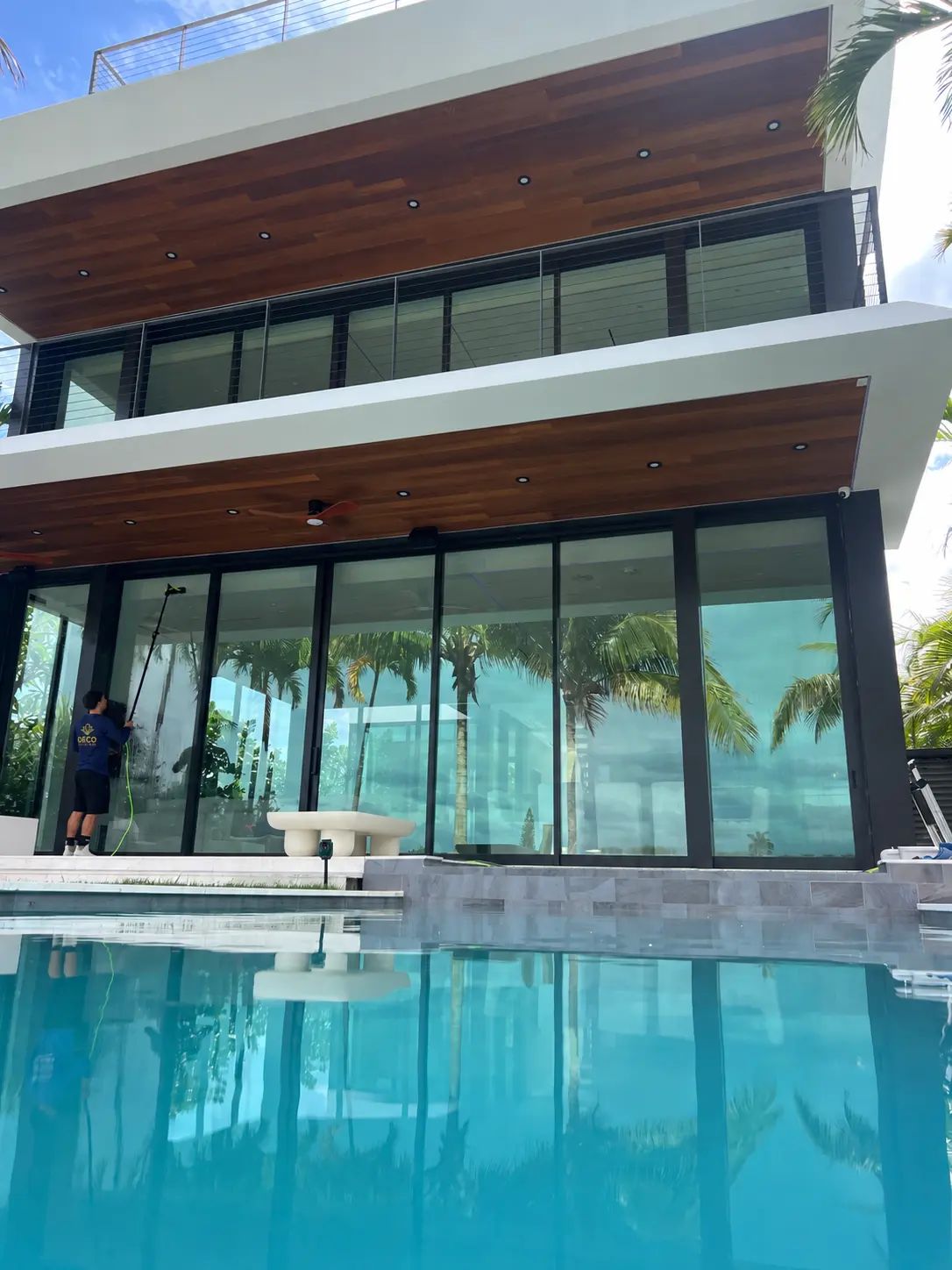 Deco Estate Care technician cleaning floor-to-ceiling glass with a pure-water pole at a waterfront home